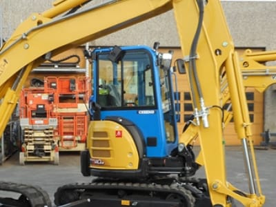 Blauw-gele minigraver met geheven graafarm voor een bedrijfsloods